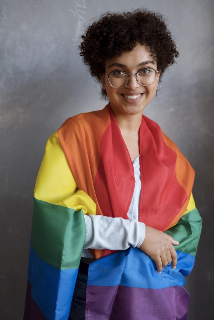 Pessoa trans do sexo feminino coberta com a bandeira da orgulho gay